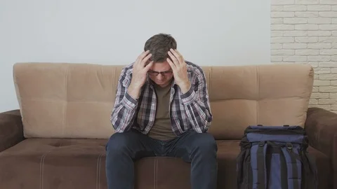 Middle-aged man sitting on the couch clasped his head. Next to him is a large Stock Footage 104798012