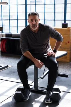 Middle-aged man sitting on flat workout bench in gym, wearing henley, Stock Photos