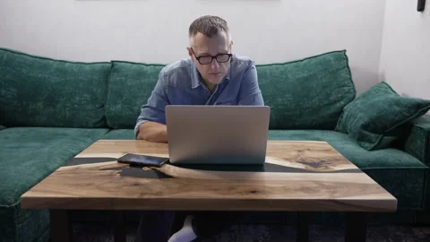 Middle-aged man sitting on a green sofa while using a laptop Video stock 171920225