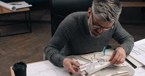 Middle aged Man sitting at his Office and Measures with the ruler his Wooden Stock Footage 126246030