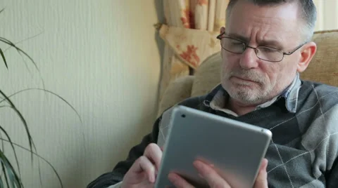Middle aged man sitting at home using tablet computer Stock Footage 33213280