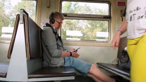 Middle-aged man is sitting on public transport with headphones and using phone. Stock Footage 159663573