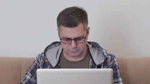 A middle aged man sitting on a sofa uses a laptop computer 스톡 동영상 104593610