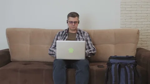 A middle-aged man sitting on a sofa with headphones in his ears is using a Stock Footage 104785693