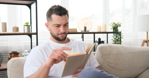 Middle aged man sitting on a sofa reading a book at home Stock Footage 150018766