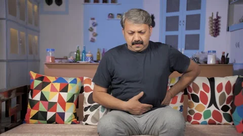 A middle-aged man sitting on a sofa facing abdominal pain - fried food diet Stock Footage 154022097