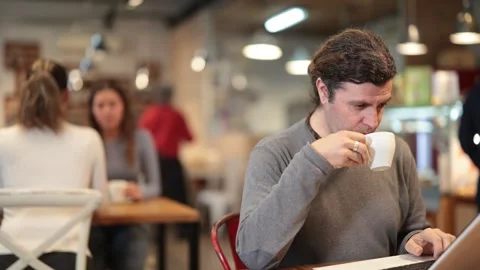 Middle-aged man sitting at table, using laptop and enjoing cup of tea in coffee Stock Footage 341427510
