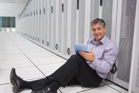 Middle-aged man sitting on tile floor in server room wearing shirt holding blue Stock Photos
