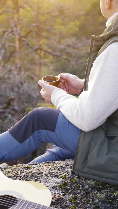 A middle-aged man is sitting on top of a cliff enjoying the sunset Stock Footage 303781946