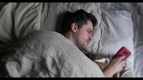 Middle-aged man sleeps in bed with his dog when a phone call wakes him up Stock Footage 301811210
