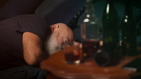 Middle-aged man sleeps beside liquor bottles, struggling with problems Stock Footage 346714349