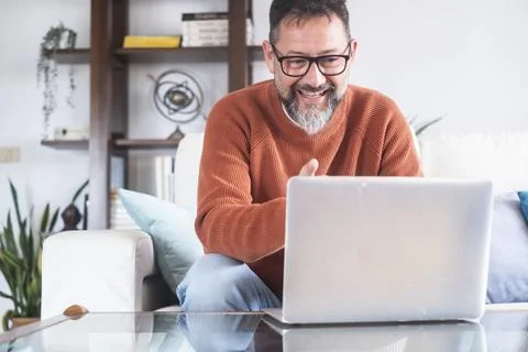Middle-aged man smiling during a video call on laptop while working remotel.. Stock Photos