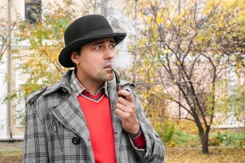 A middle-aged man smokes a pipe in a city park. Stock Photos