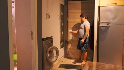 Middle aged man spraying cleaner on mirror in bathroom, cleaning routine using Stock Footage 333578447