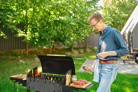Middle-aged man sprinkles raw steak with oil at backyard Foto stock