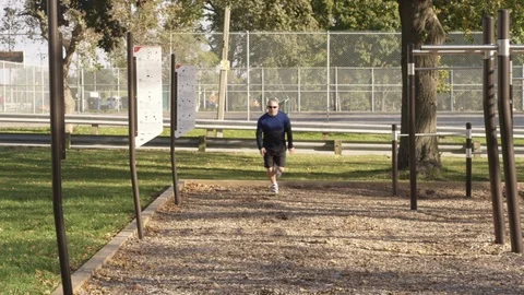 A middle aged man sprints towards the camera at an exercise park - slow motion - Stock Footage 123487268