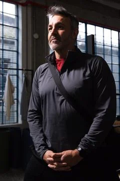 Middle-aged man standing in converted warehouse gym near windows, wearing Stock Photos