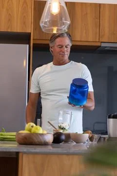Middle-aged man standing at kitchen island in modern home, holding blue jar with Stock Photos
