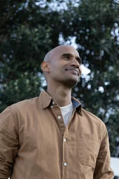Middle-aged man standing in park wearing tan button-up shirt with chest pocket Stock Photos