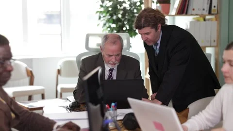 Middle aged man stands near table and helps an elderly employee with the Stock Footage 341383971