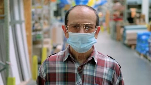 A middle-aged man stands in a shop wearing a mask and looks at the camera Stock Footage 147677789