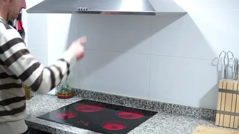 Middle aged man switches off extractor light and ceramic stove to save Stock Footage 219436698