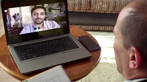 Middle aged man taking notes in a video call he's having with younger colleag Stock Footage 131196384