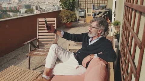 Middle-aged man taking selfie while sitting on balcony Video stock 229507523