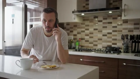 A middle-aged man talking on his mobile phone and smiling while eating panc.. Stock Footage 332287845