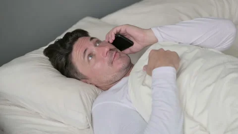 Middle Aged Man Talking on Smartphone Laying in Bed Video stock 142376543