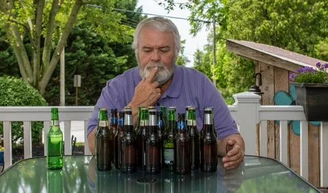 Middle-aged Man Thoughtfully Examines Empty Beer Bottles at Outdoor Table i.. Stock Photos