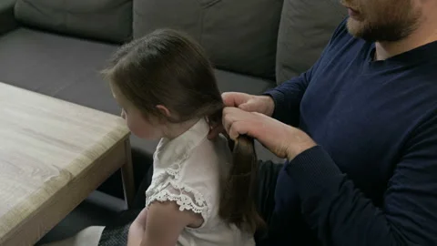 Middle-aged man tries to braid his little daughter's braids. He's bad at it Stock Footage 147440482