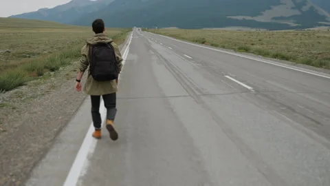Middle-aged man is trying to stop passing car on road in mountains. Video stock 280887625