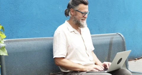 Middle-aged man typing on a laptop sitting on a bench in the street. Stock Footage 165182204