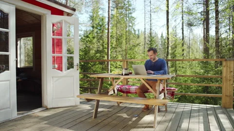 Middle aged man typing on laptop computer sitting on wooden porch in countryside Stock Footage 195357901