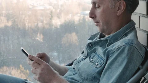 A middle aged man uses a smartphone. He is studying various programs. close-up Video stock 99174824