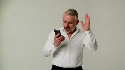 A middle aged man uses a smartphone, expresses ire and dissatisfaction, talks Stock Footage 253258301
