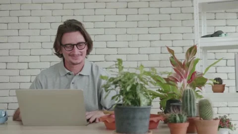 A middle-aged man is using a laptop computer with plants in the foreground. Stock Footage 141126422
