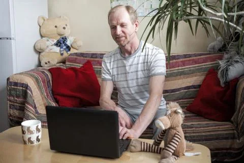 Middle aged man using a laptop computer sits at home at the table, on sofa Stock Photos