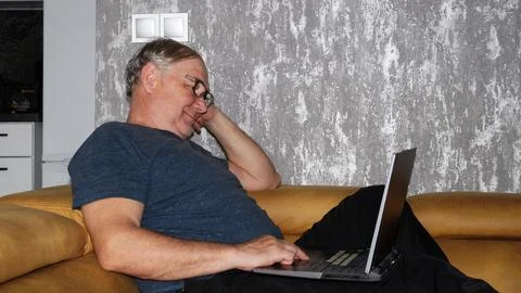 Middle aged man using laptop while relaxing on sofa at home interior Stock Photos