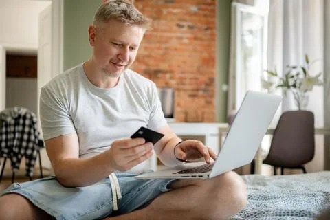 Middle aged man using laptop and credit card on bed in home Stock Photos