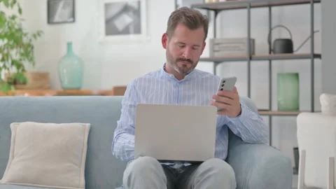 Middle Aged Man Using Phone with Laptop in Lap 스톡 동영상 287898306