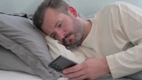 Middle Aged Man Using Phone while Lying on Side in Bed Stock Footage 287899292