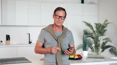 Middle aged man using smart phone and showing approval sign ok In bright home Video stock 231704031