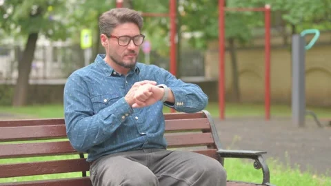 Middle Aged Man Using Smart Watch on Park Bench Video stock 311359877