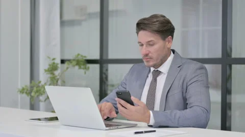 Middle Aged Man using Smartphone while using Laptop in Office Video stock 162846165