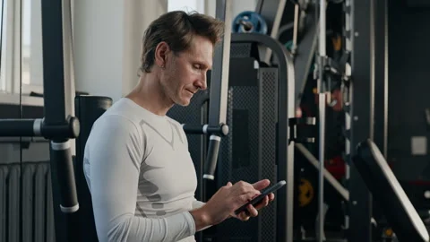 Middle Aged Man Using Smartphone for Workout Tracking in Gym Stock Footage 345200446