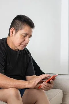 Middle aged man using smartphone on couch showing everyday technology use a.. Stockfoto's