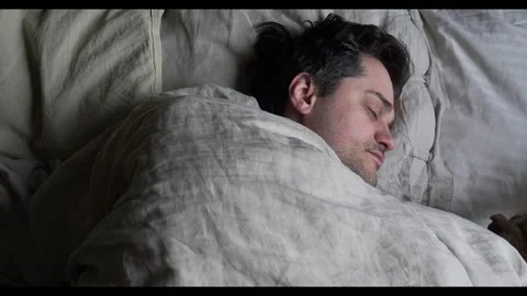 Middle-aged man wakes up in bed with his dog, enjoying a cozy morning moment Stock Footage 301810900