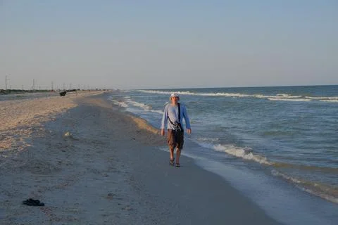 Middle-aged man walking along the seashore in summer with camera and taking Stock Photos